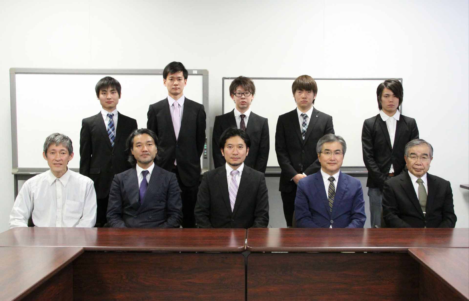 前列左から大東文化大学環境創造学部長山口由二,DNPメディアクリエイト第2企画本部長原慎一氏,大東文化大学環境創造学部飯塚裕介,DNPメディアクリエイト取締役執行役員佐々木誠氏,大東文化大学学長太田政男。後列は飯塚裕介ゼミの学生(井野雄太,内山翔大,川村能勝,末永真樹,中谷友紀)。